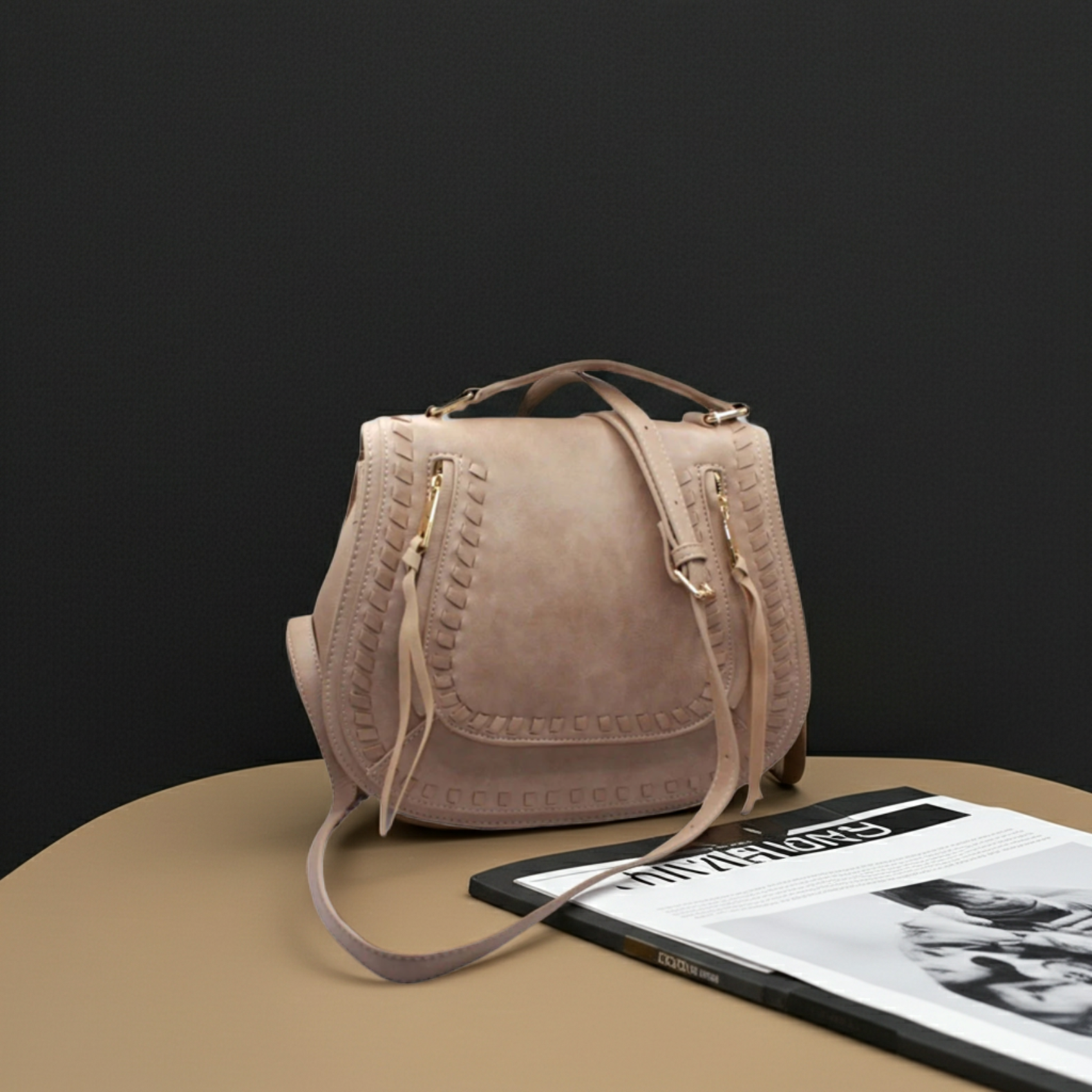 Beige handbag on a table with a magazine underneath against a black background