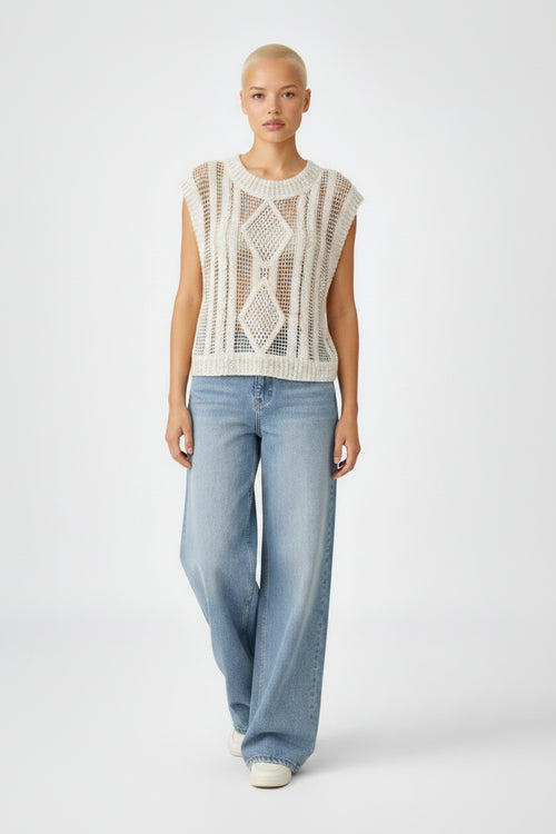 Woman wearing a sleeveless crochet top and blue jeans on a white background