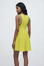 Woman wearing a yellow dress with cut-out shoulders against a white background